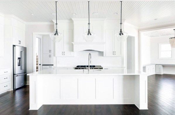 Modern kitchen with sleek white cabinetry and small pendant lights hanging above a pristine white island, featuring dark wood flooring