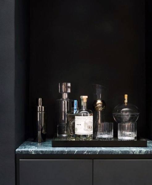 Sleek mini bar with black backdrop, marble countertop, and elegant glassware and bottles.