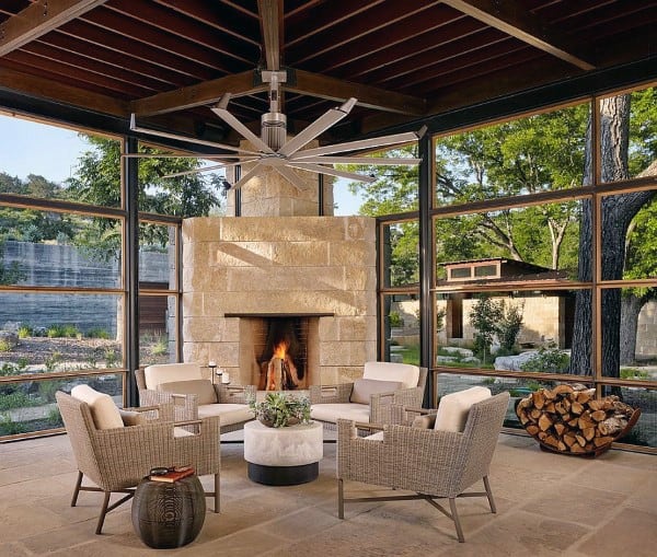 Modern sunroom with stone fireplace, wicker chairs, wood ceiling, and scenic windows.