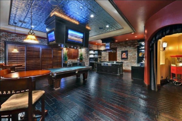 Spacious game room with pool table, dark wood flooring, brick walls, and ceiling-mounted TVs.