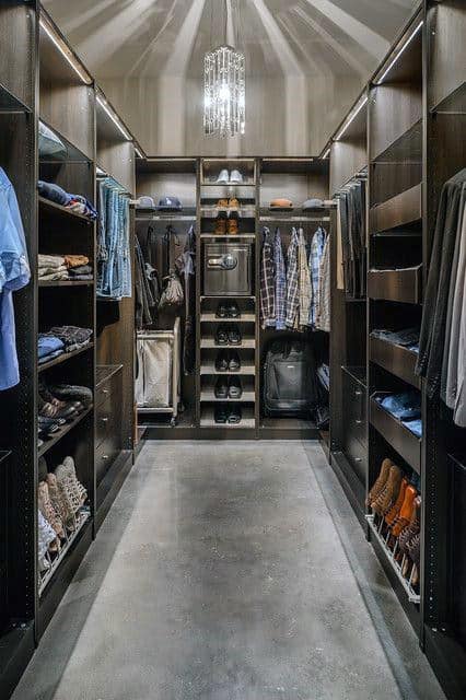 Luxurious walk-in closet with wooden shelves, clothing, shoes, and a modern chandelier overhead