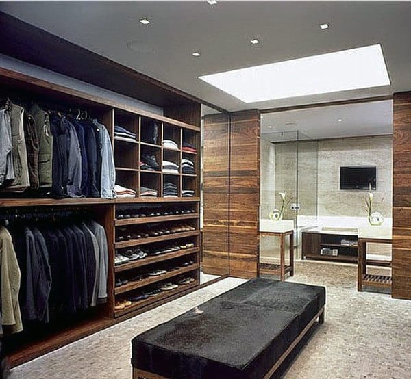 Walk-in closet with neatly arranged clothes and shoes, a central bench, and a view into a modern bathroom