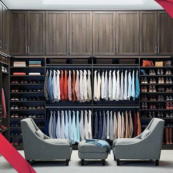 A neatly organized walk-in closet with clothes, shoes, and two gray chairs facing each other