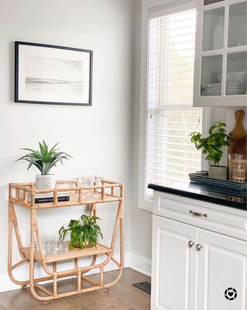 Wicker bar cart with glassware and plants in a bright white kitchen corner.