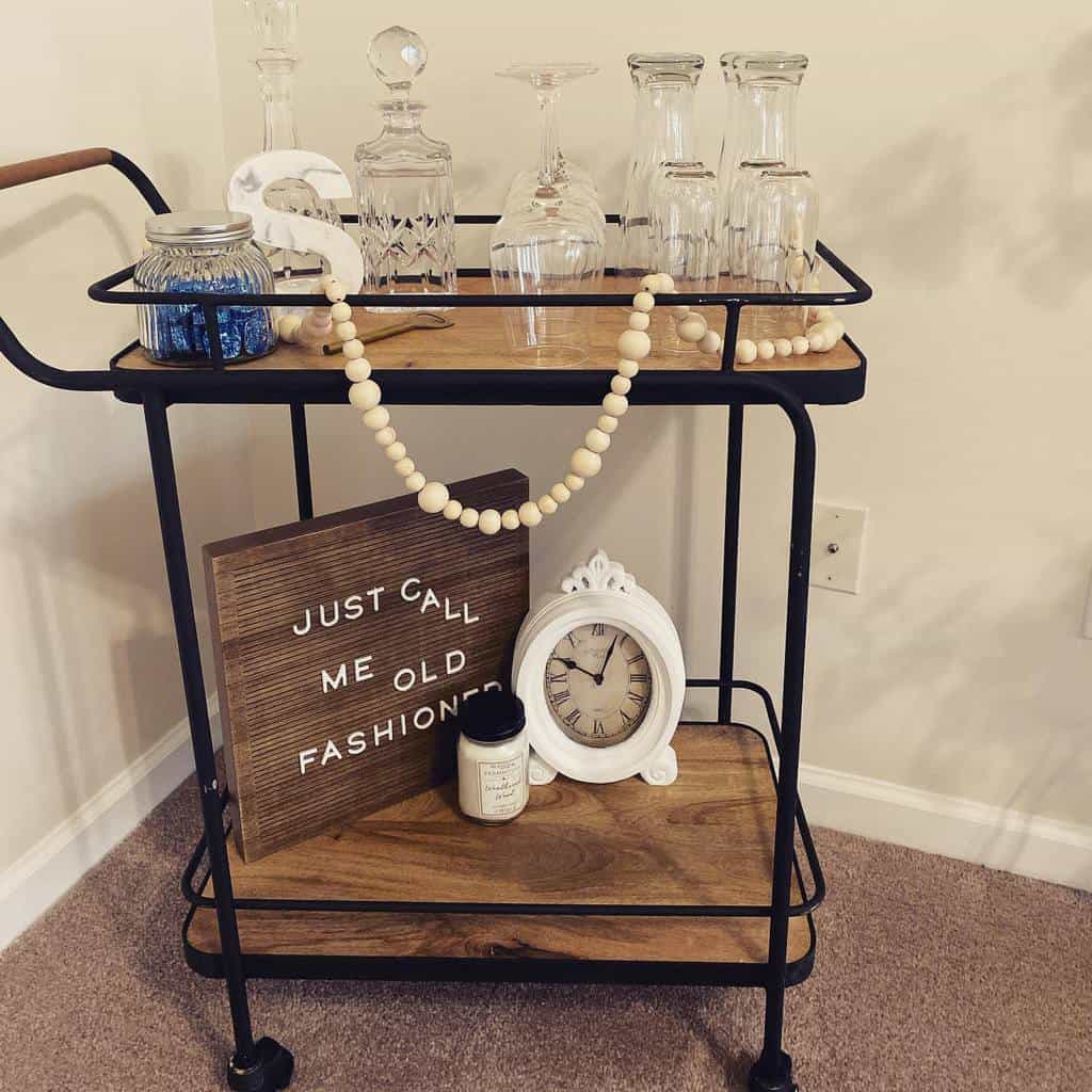 Wooden bar cart with crystal glassware, decorative sign, and vintage clock.