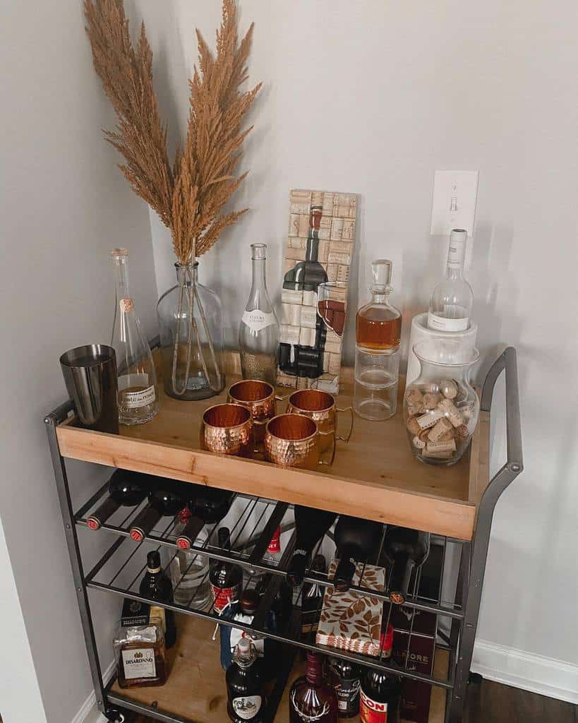 Wood and metal bar cart with liquor bottles, copper mugs, and decorative pampas grass.