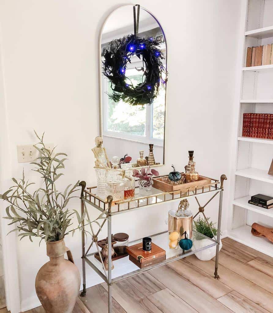 Classic bar cart with crystal decanters, decorative pumpkins, and a mirror with a wreath.