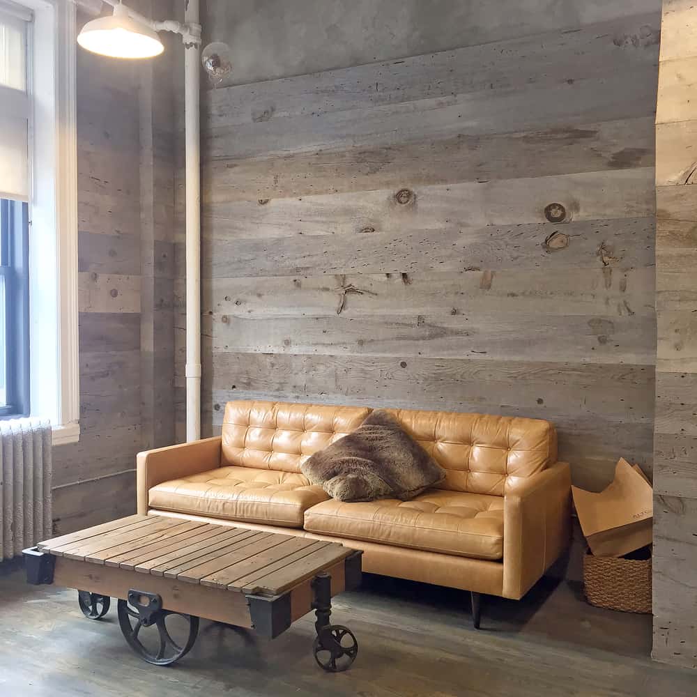 Loft-style room with a brown leather sofa, rustic wood coffee table, and gray wooden walls