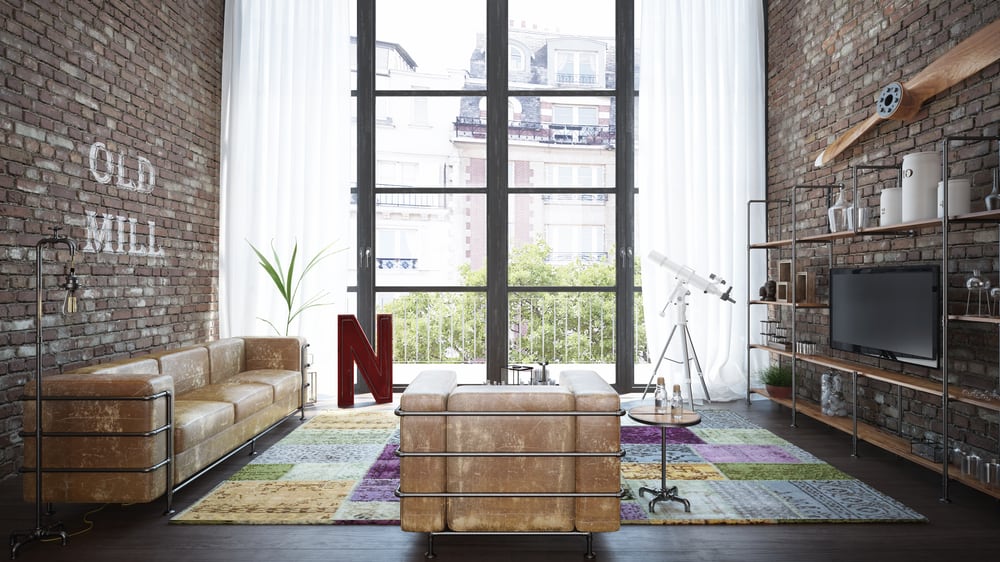 Loft with brick walls, large window, brown leather furniture, colorful rug, telescope, and decorative bookshelf