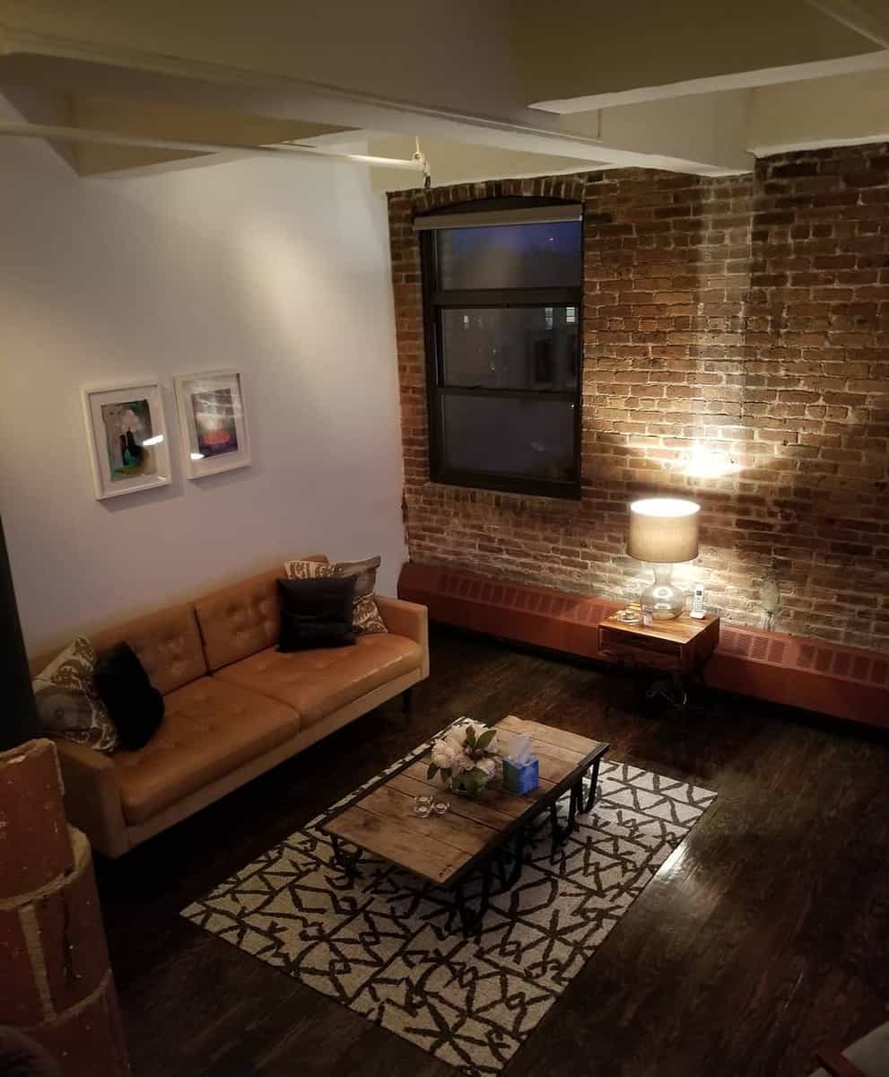 Cozy loft with exposed brick, a plush brown sofa, patterned rug, and wooden coffee table under warm lighting