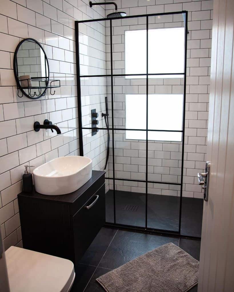 Small industrial bathroom with black-framed shower, white subway tiles, and vessel sink.