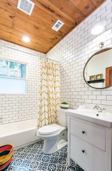 Bathroom with white subway tiles, wooden ceiling, patterned floor, round mirror, and yellow/white shower curtain