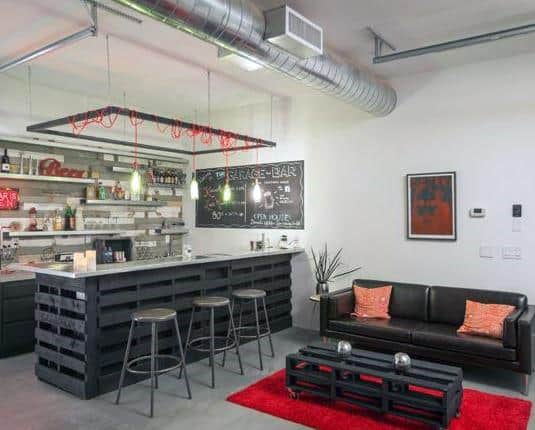 Modern garage bar with pallet-style counters, industrial stools, and cozy lounge seating.