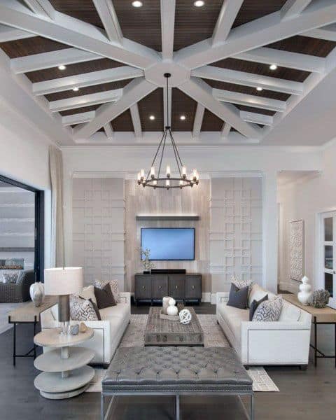 Modern living room with geometric ceiling, white sofas, a chandelier, and a TV on the wall