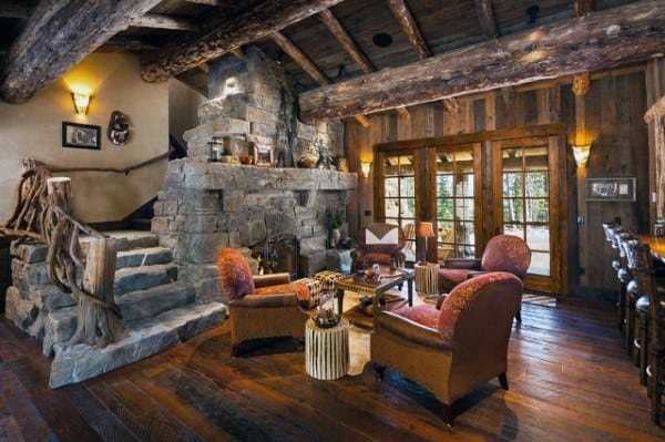 A rustic living room featuring a stone fireplace, wooden beams, a staircase with natural wood accents, and cozy seating, creating a warm and inviting space