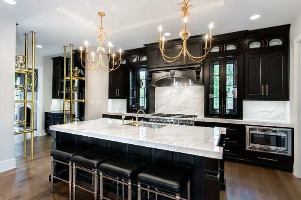 Luxurious black kitchen cabinets with marble countertops, chandeliers, and black bar stools.