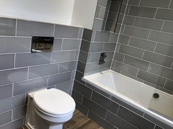 Modern bathroom with grey tile walls, featuring a sleek toilet and bathtub