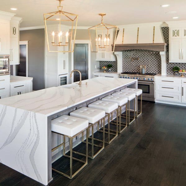 Elegant kitchen featuring gold chandeliers above a spacious white marble island with modern gold-accented stools and sleek cabinetry