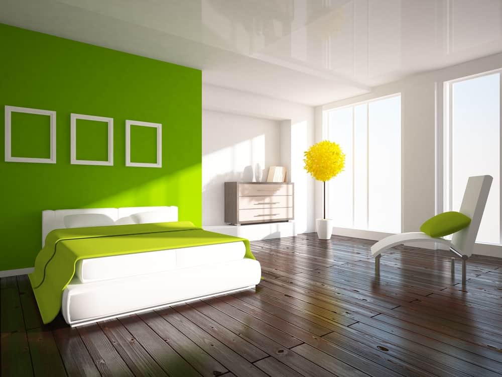 Modern bedroom with green accent wall, bed, chair, and bright yellow floor lamp on wooden flooring