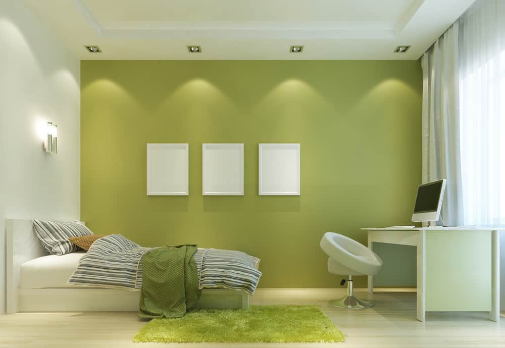 Minimalist bedroom with green accent wall, bed, desk, chair, and three white frames featuring natural light from window