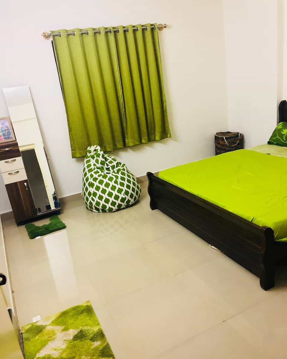 Bedroom with green decor: bed, curtains, bean bag, and rug; white walls, a dresser, and a mirror are visible