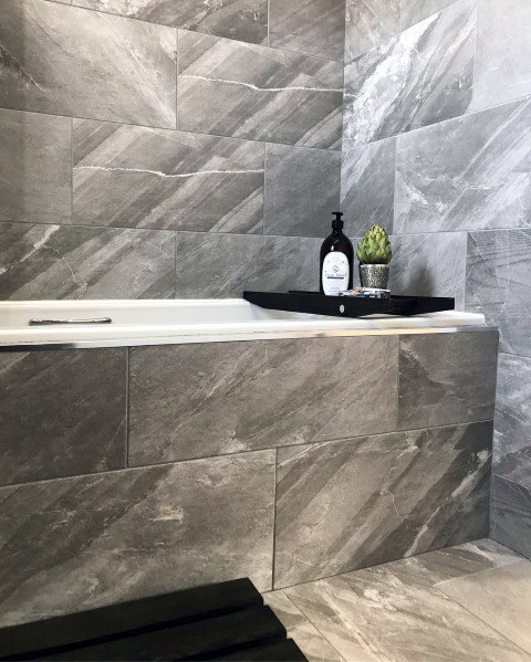 Modern bathroom with grey stone tiles, black tray, and bottle near bathtub edge