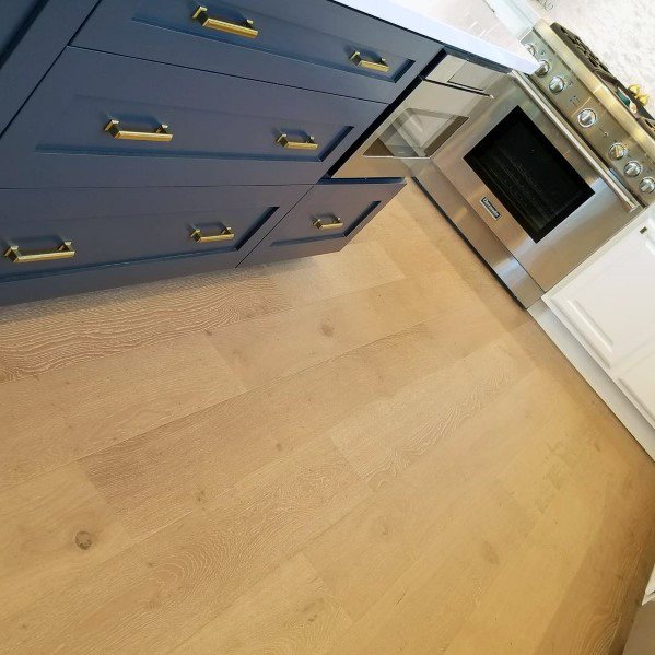 Charming kitchen with light hardwood flooring, navy blue cabinetry, and modern stainless steel appliances, enhanced by elegant gold handles