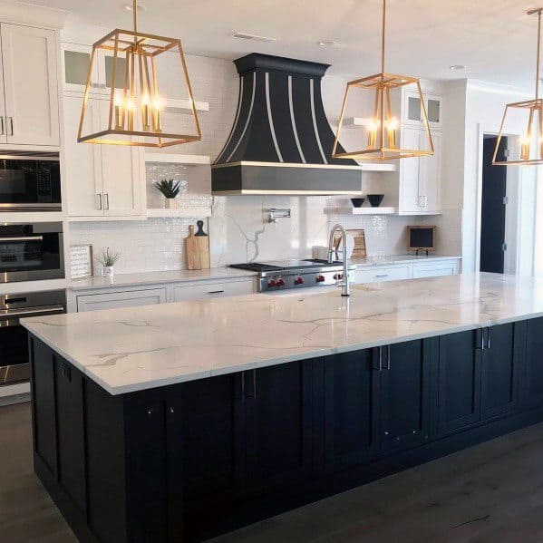 Modern kitchen with gold-framed pendant chandeliers above a white and black marble island, complemented by sleek cabinetry and a stylish range hood