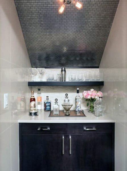 Stylish mini bar with dark cabinetry, mirrored backsplash, glassware shelf, and floral decor.