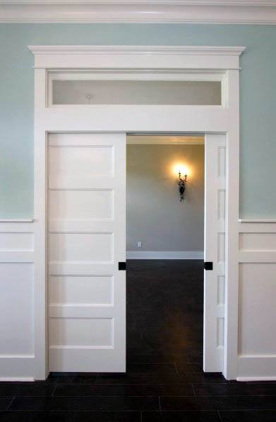 Elegant white double pocket doors with panel detailing and transom window, opening to a room with soft lighting and dark flooring