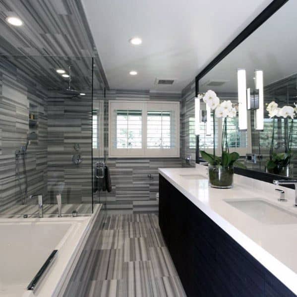 Modern bathroom with striped gray tiles, large mirror, bathtub, and orchids on the counter