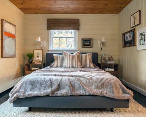 Cozy bedroom with a double bed, striped pillows, art on walls, and a window with a wooden blind