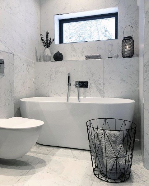 Modern bathroom with a white tub, black wire basket, decorative vases, and a window with natural light