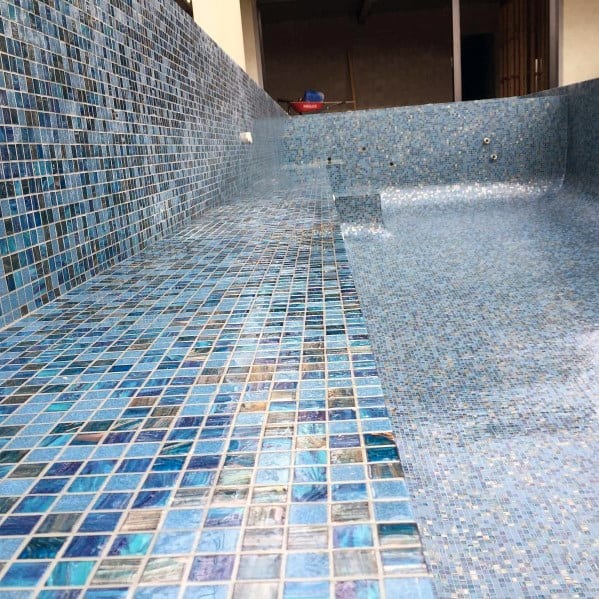 Empty swimming pool with vibrant blue iridescent mosaic tiles creating a shimmering effect.