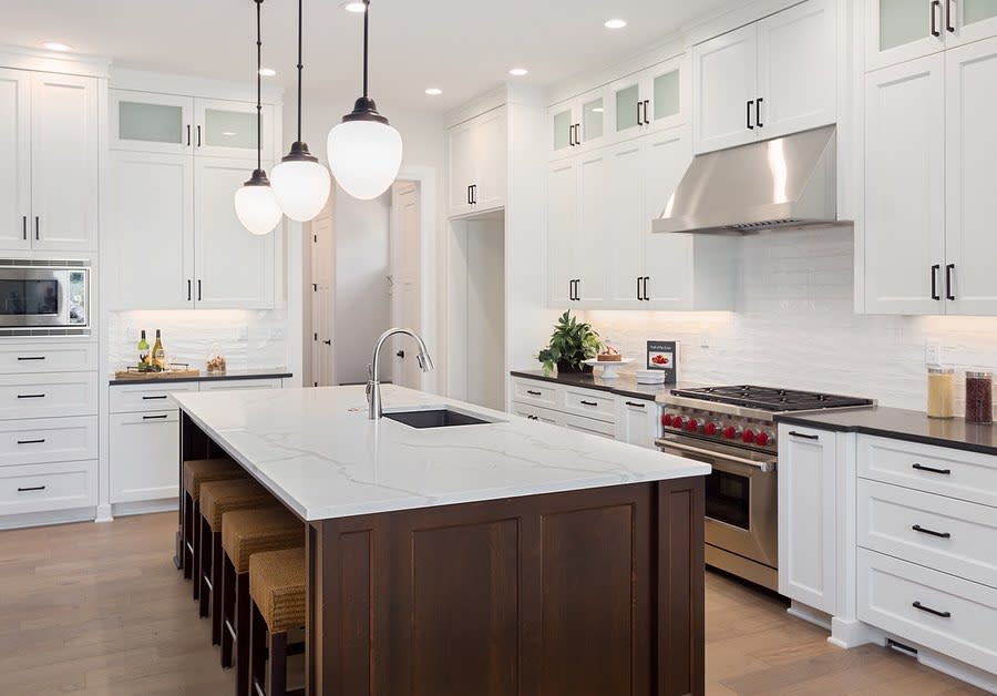 Large white kitchen with marble-topped island, dark wood base, and pendant lighting.