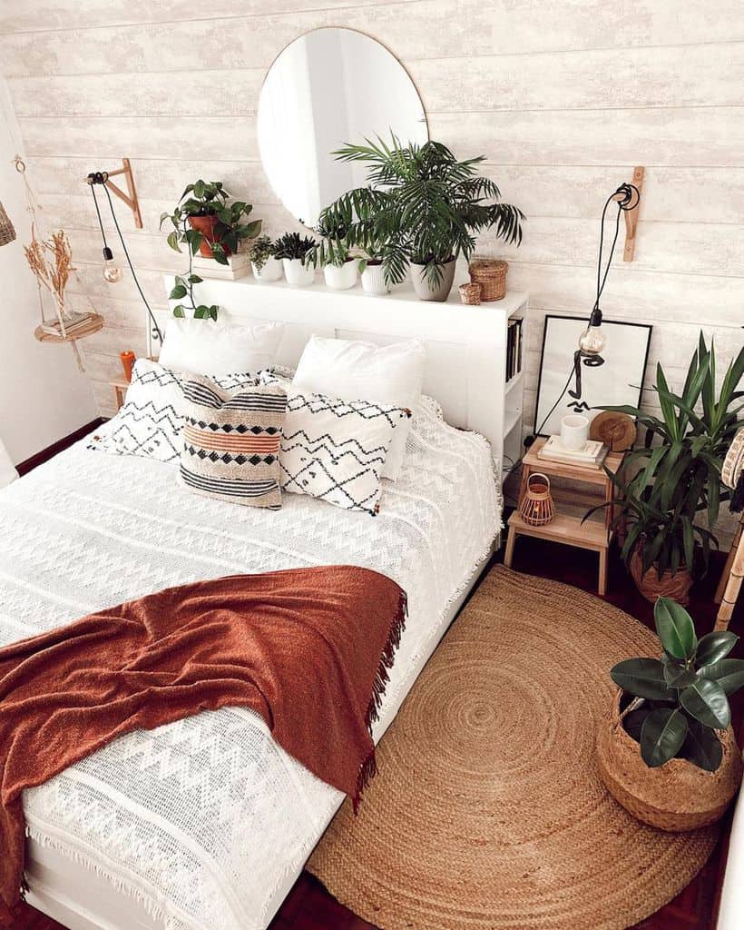 Boho bedroom with lush indoor plants, woven accents, patterned pillows, and a cozy white bedspread.