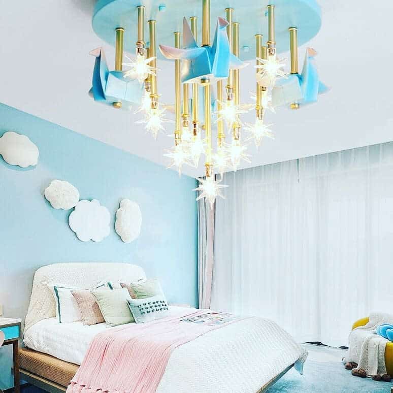 Kids' room with blue walls, cloud wall art, pastel bedding, and star-shaped chandelier.