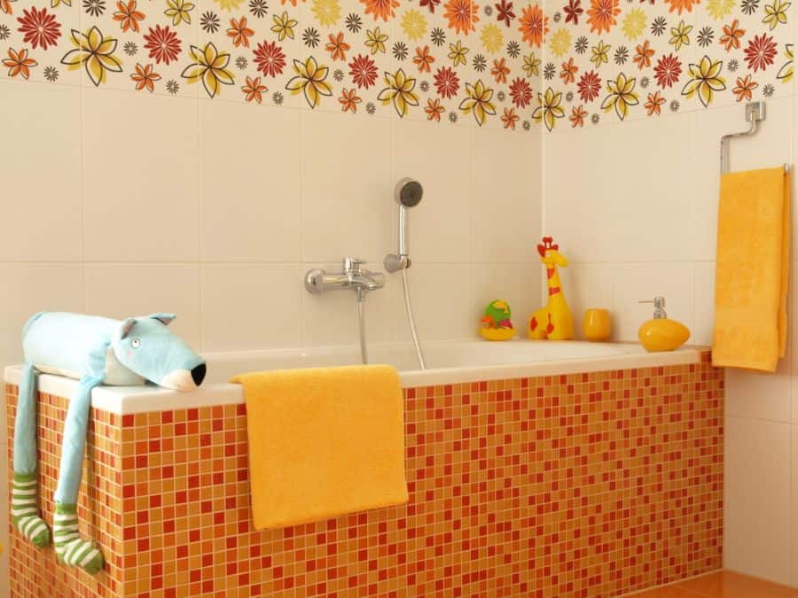 A colorful bathroom with a bathtub, orange tiles, stuffed toys, and floral wallpaper