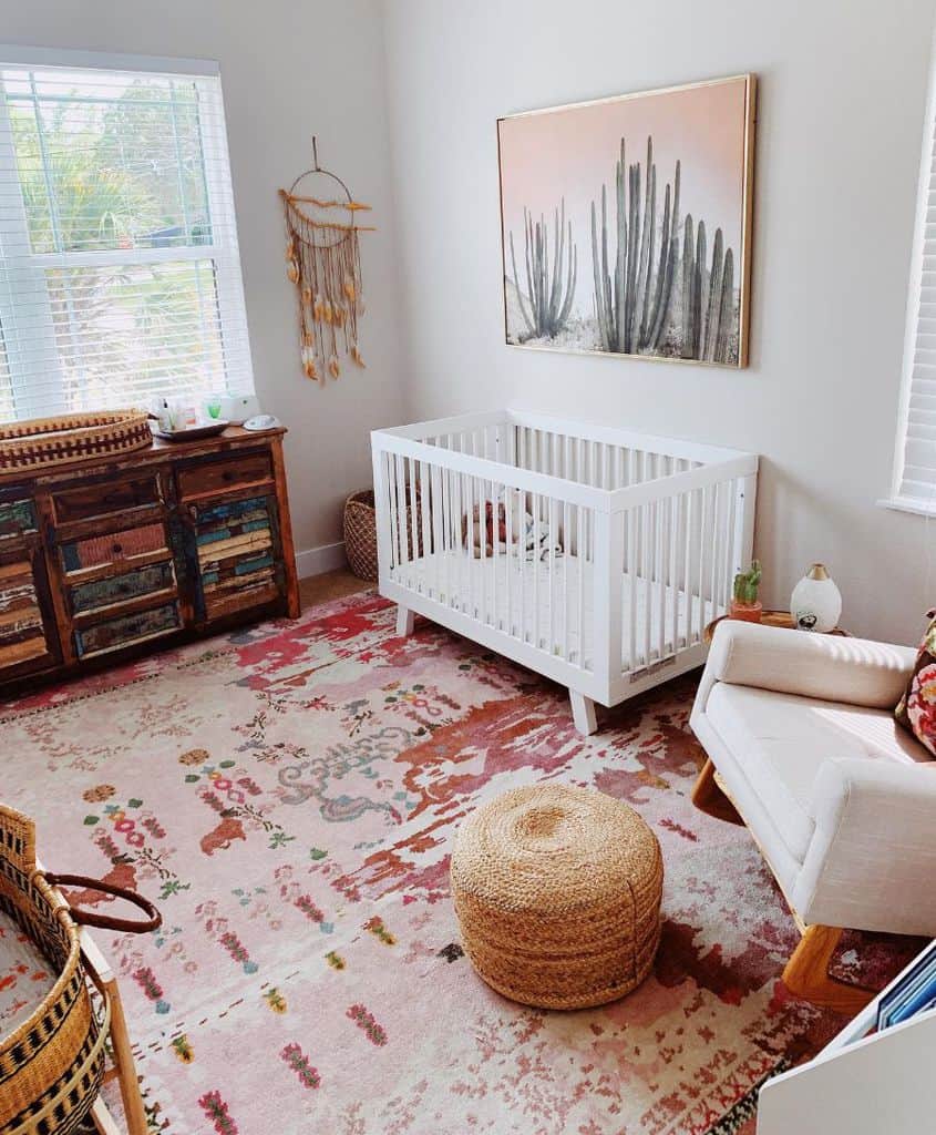 Boho nursery with cactus artwork, white crib, woven accents, and colorful patterned rug.