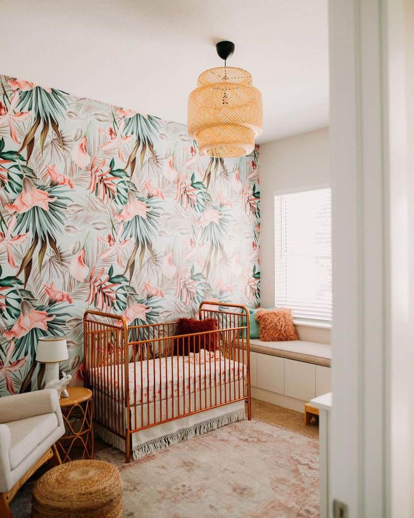 Boho nursery with tropical wallpaper, copper crib, woven lighting, and cozy seating nook.