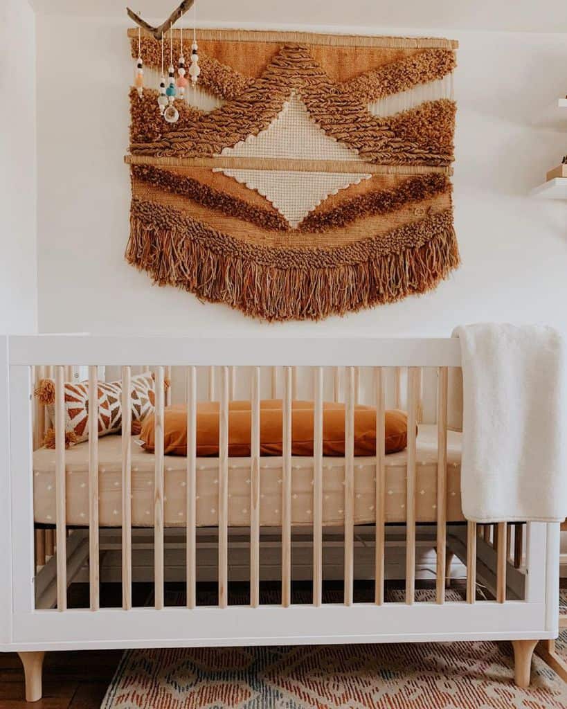 Boho nursery with woven wall hanging, white crib, warm earthy tones, and cozy patterned bedding.