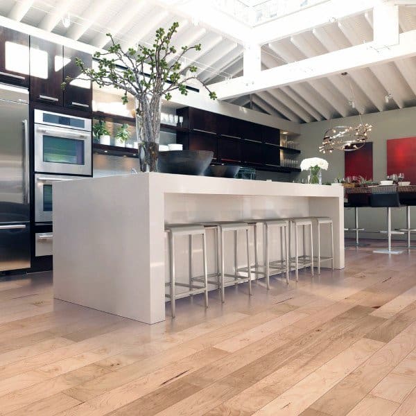 Modern kitchen with a spacious white island, bar stools, wooden floors, and plants under a skylight-adorned ceiling