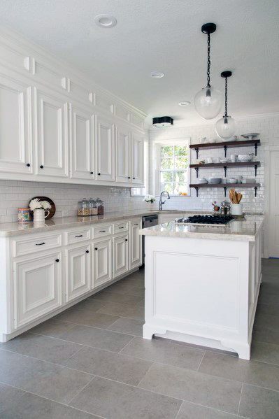 Bright kitchen with white cabinetry, a marble countertop island, subway tile backsplash, and gray tile flooring, creating a clean, modern aesthetic