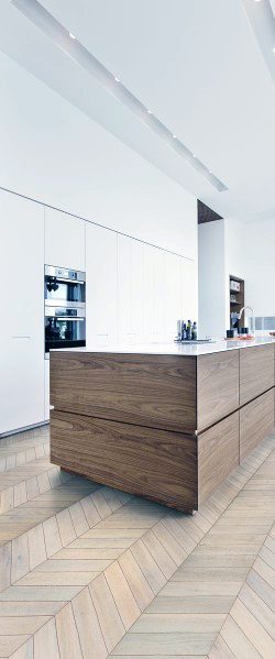 Minimalist kitchen with herringbone hardwood flooring, modern wood-textured cabinetry, and a sleek white marble countertop island, creating a clean and contemporary design