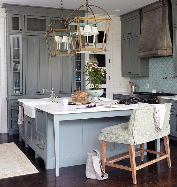 Charming kitchen with light blue cabinetry, dark hardwood flooring, a marble countertop island, and unique brass light fixtures, offering a cozy and elegant atmosphere