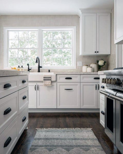 Charming kitchen with dark hardwood flooring, white cabinetry, a marble countertop, and a cozy rug, offering a bright and inviting atmosphere with natural light