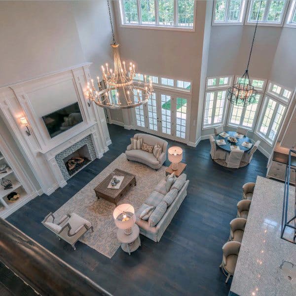 Spacious living room with high ceilings, chandeliers, sofas, a fireplace, and a dining area with large windows