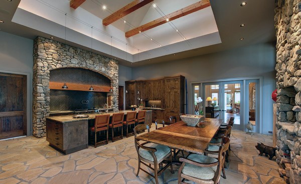 Rustic kitchen with stone walls, wooden beams, island bar seating, and dining table with chairs