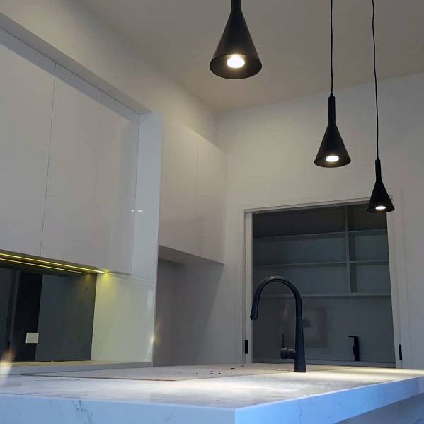 Modern kitchen with sleek black mini pendant lights above a white marble island, complemented by clean cabinetry and a minimalist design