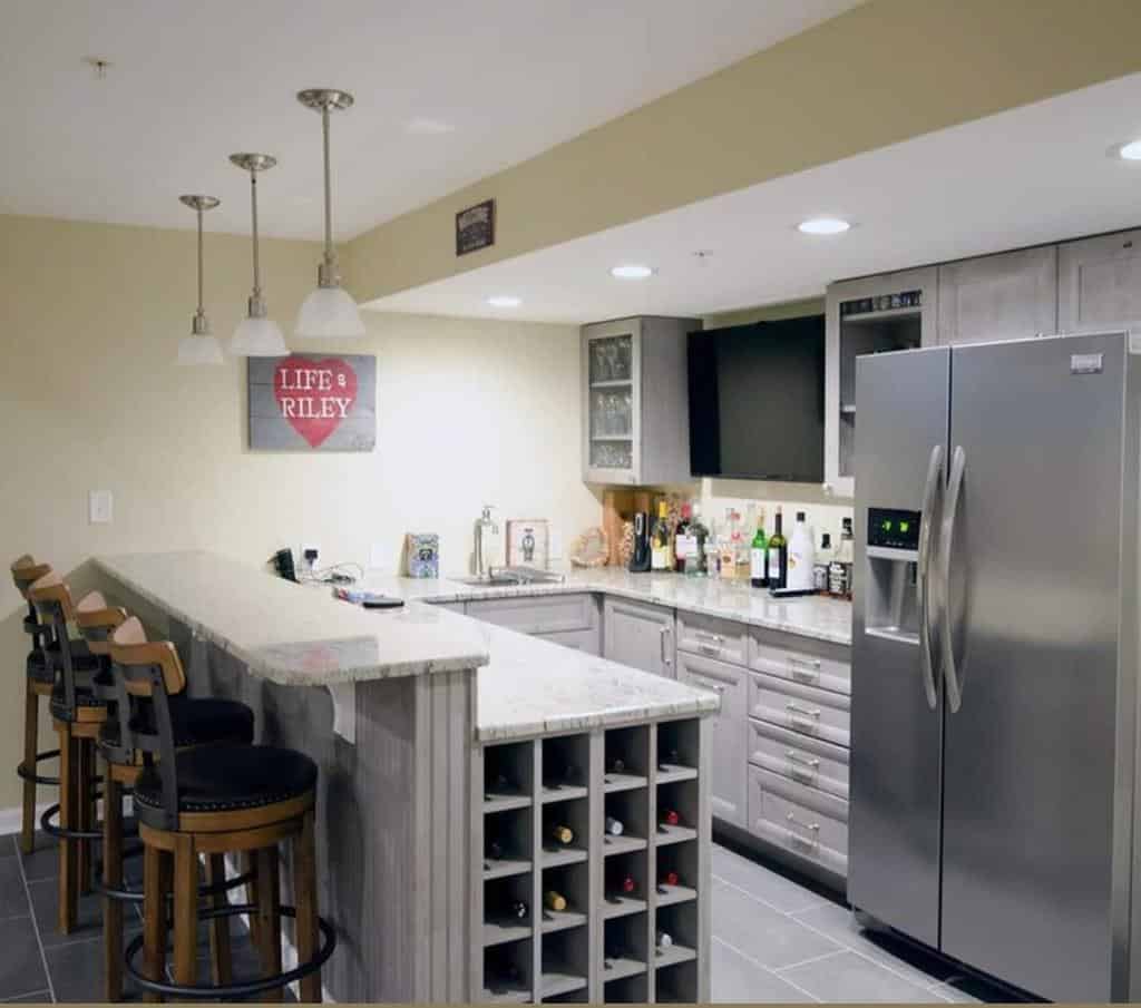 Home wet bar with gray cabinets, wine rack, stainless steel fridge, and pendant lighting.